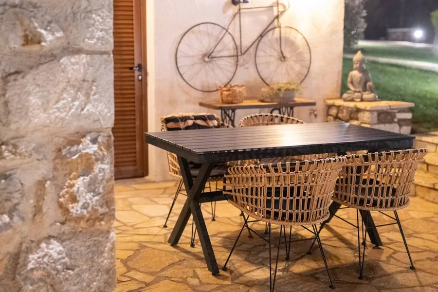 Τραπέζι με ψάθινες καρέκλες σε πέτρινο δάπεδο, με ποδήλατο στον τοίχο